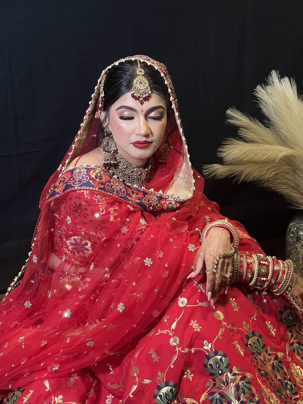 Bride in red bridal outfit with full glam makeup, seated in studio by 902 Beauty Bar, Dartmouth NS